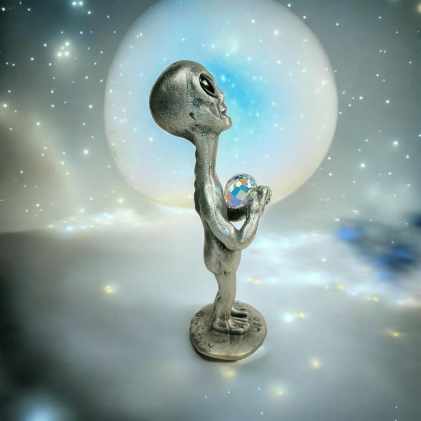 Side view of the alien figurine holding a faceted orb against a glowing, starry backdrop.