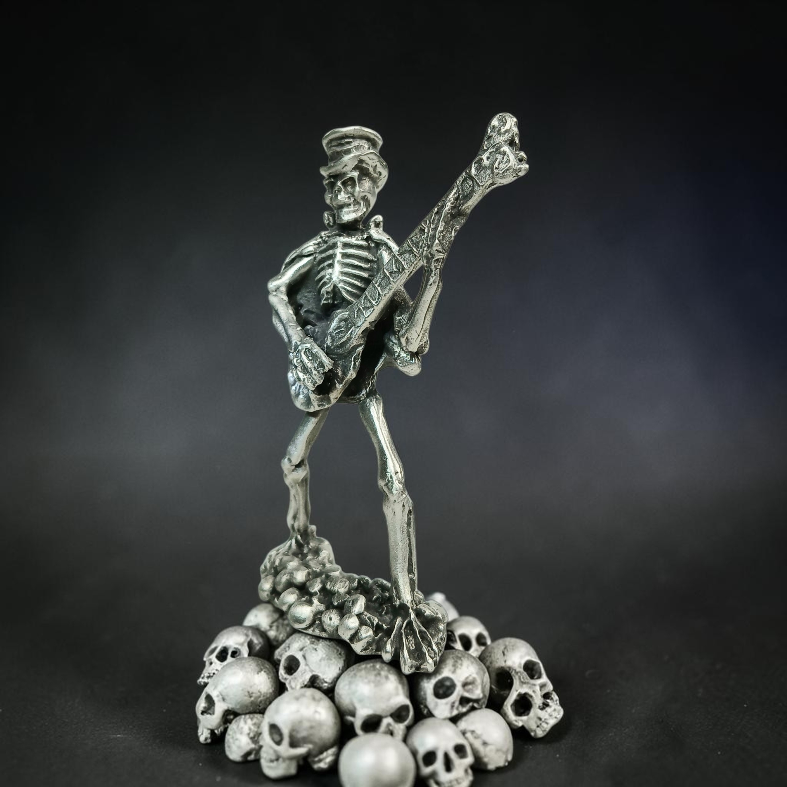 Skeleton musician wearing a hat and playing a bass guitar above a pile of skulls.