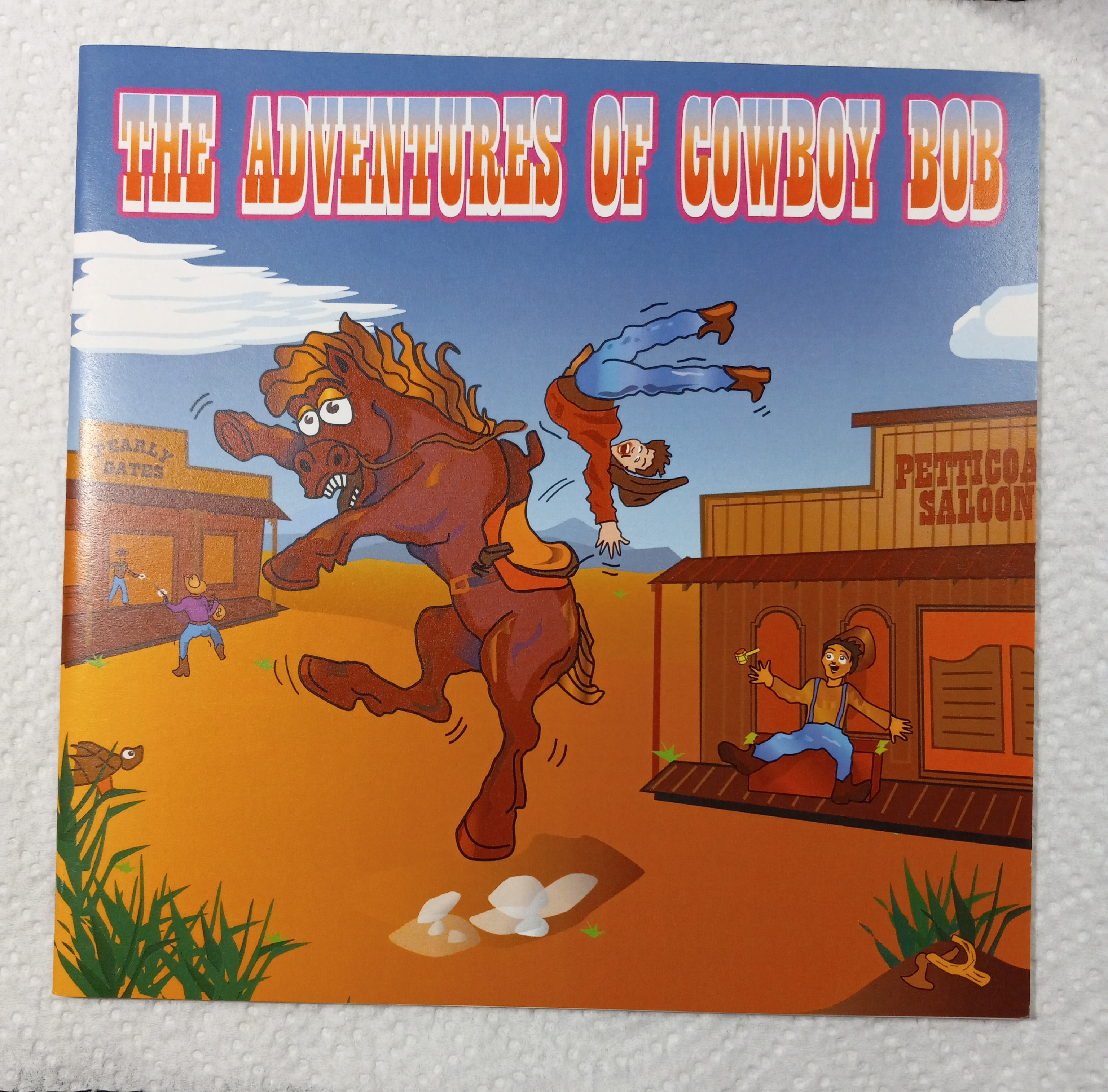The Adventures of Cowboy Bob artwork, showing a cowboy thrown from a bucking horse in a Western town.