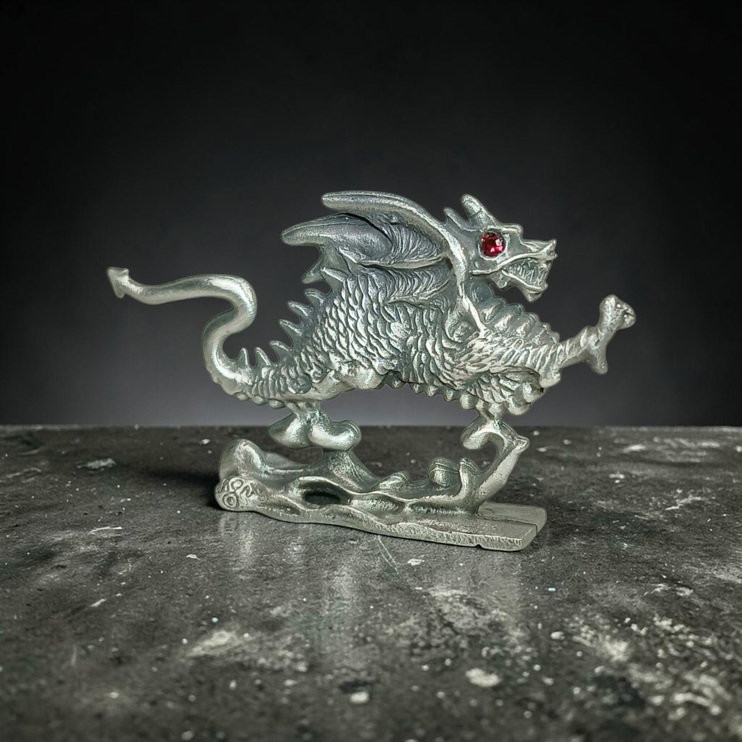 Pewter dragon sculpture with raised wings, a curled tail and a red eye.