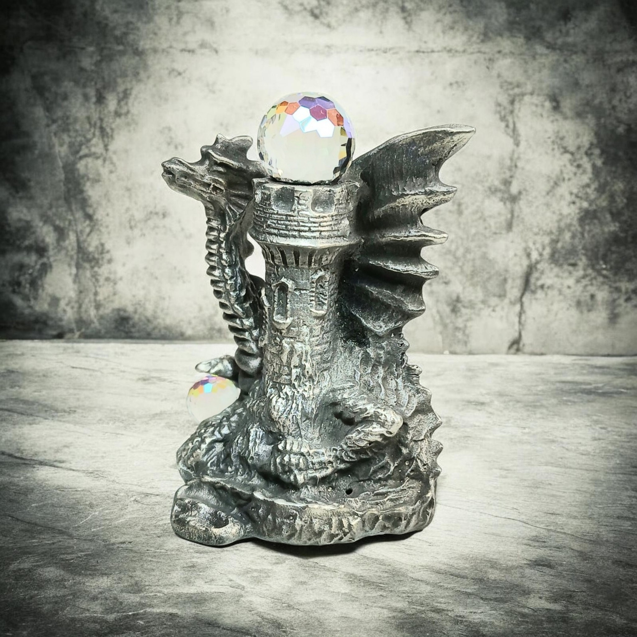Dragon sculpture curled around a stone tower with a faceted orb on top and another beside its base.