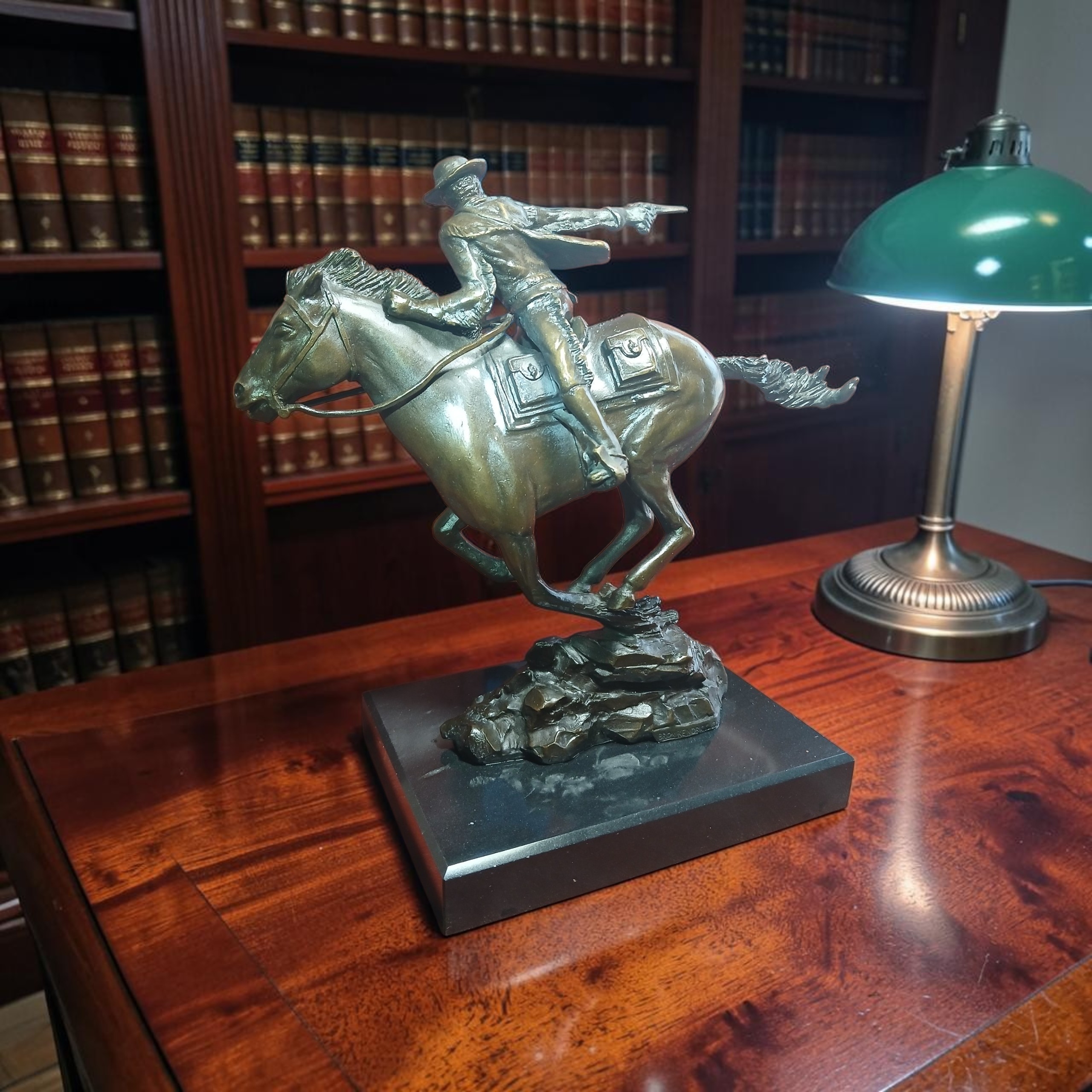 Horse-and-rider sculpture with a mounted rider holding a revolver, displayed on a desk beside a green lamp.