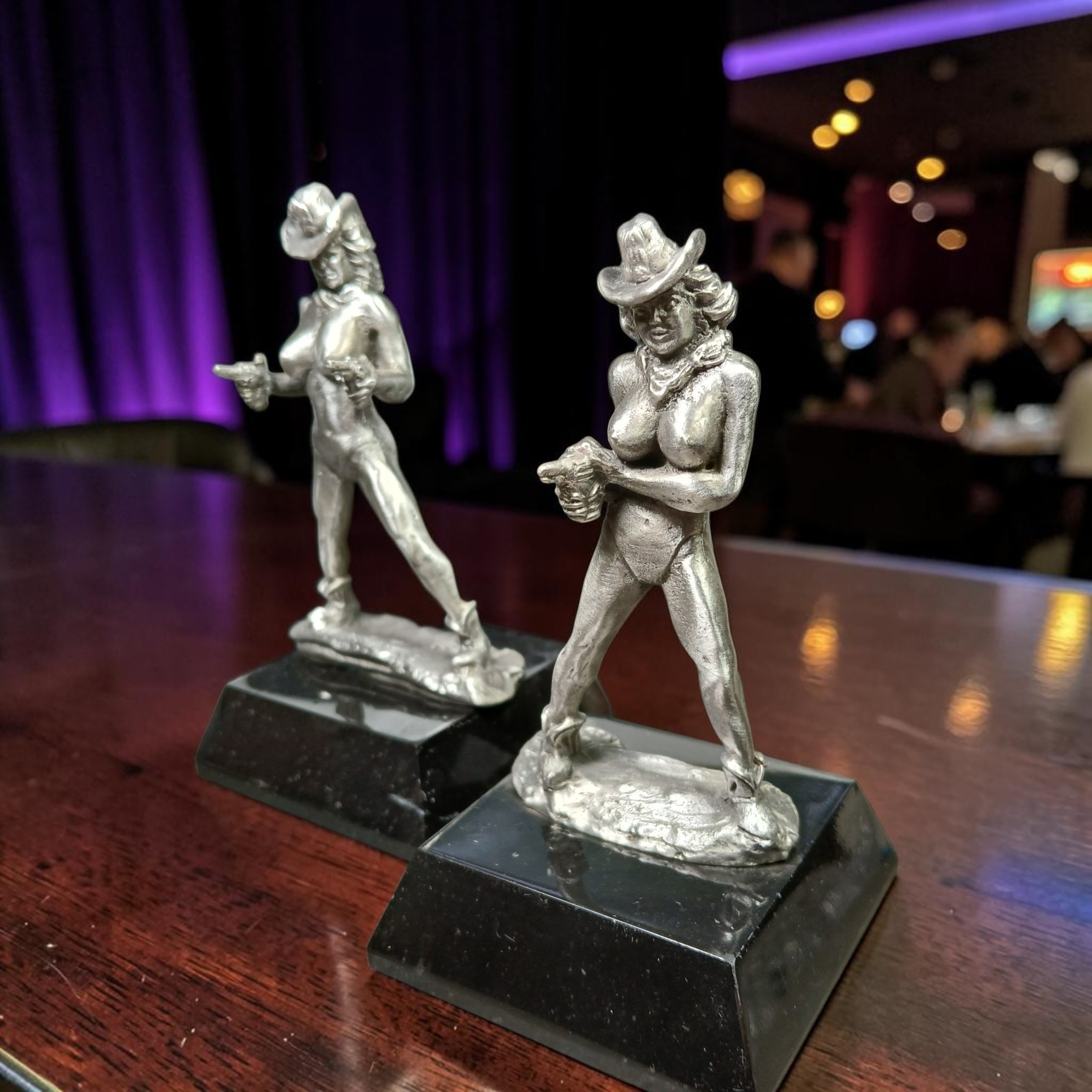 Two cowgirl figurines wearing hats and holding revolvers, displayed on black bases.