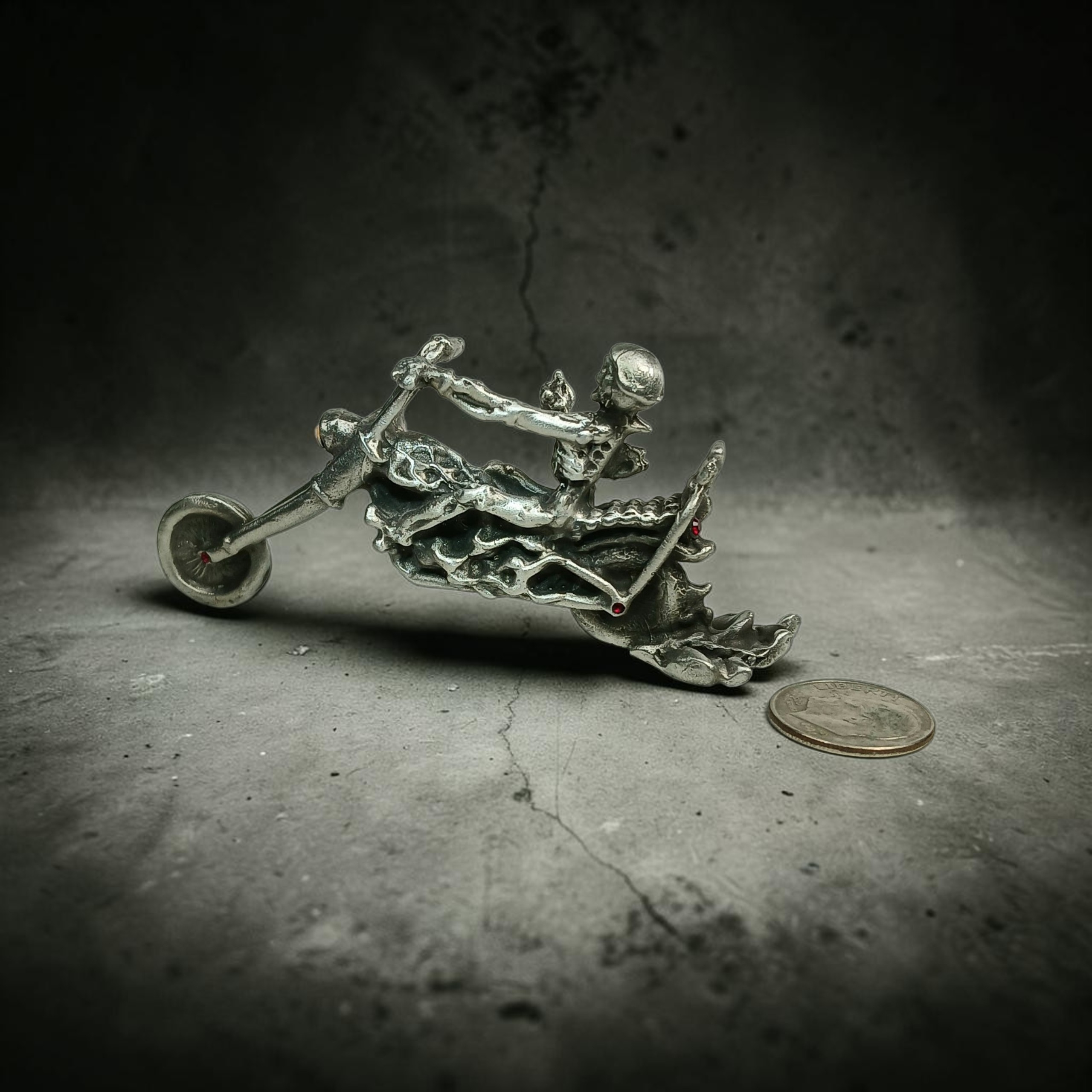 Skeleton rider on a motorcycle with a long front fork and flame-shaped bodywork, with a coin beside it for scale.