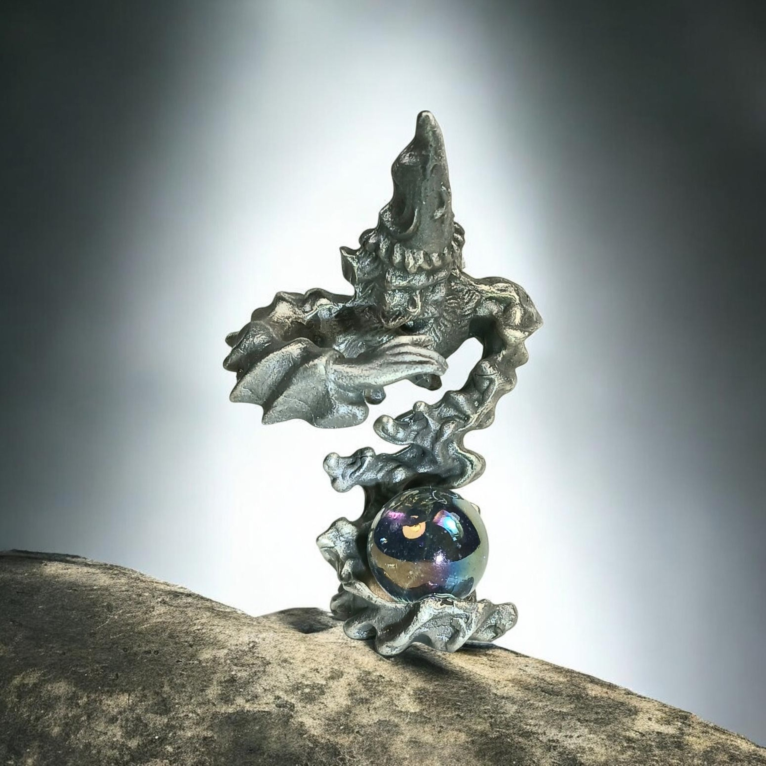 Wizard figure wearing a pointed hat and reaching forward above a reflective orb and curling base.