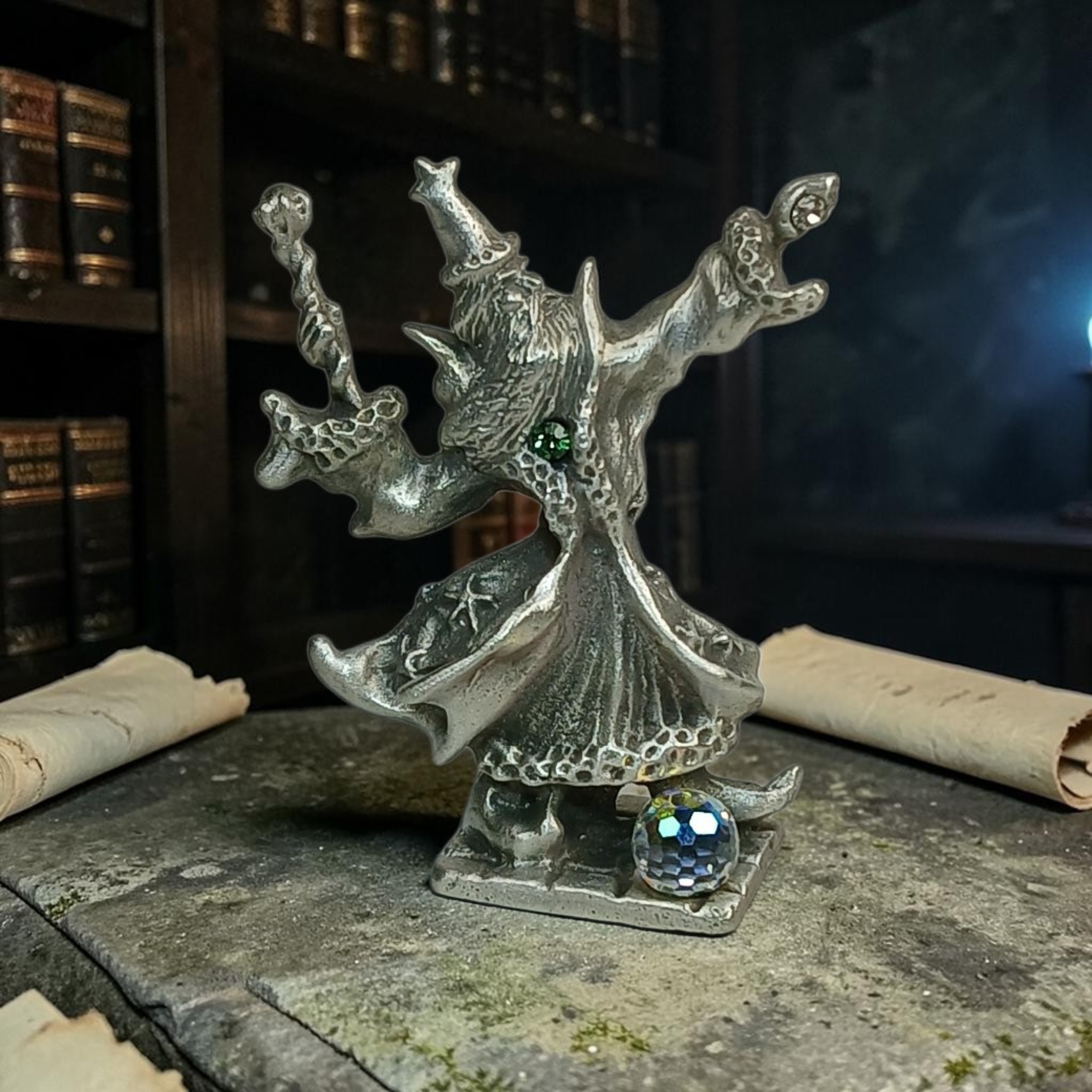 Pewter wizard with raised arms, flowing robes, a green accent and a faceted crystal orb, displayed among books and scrolls.
