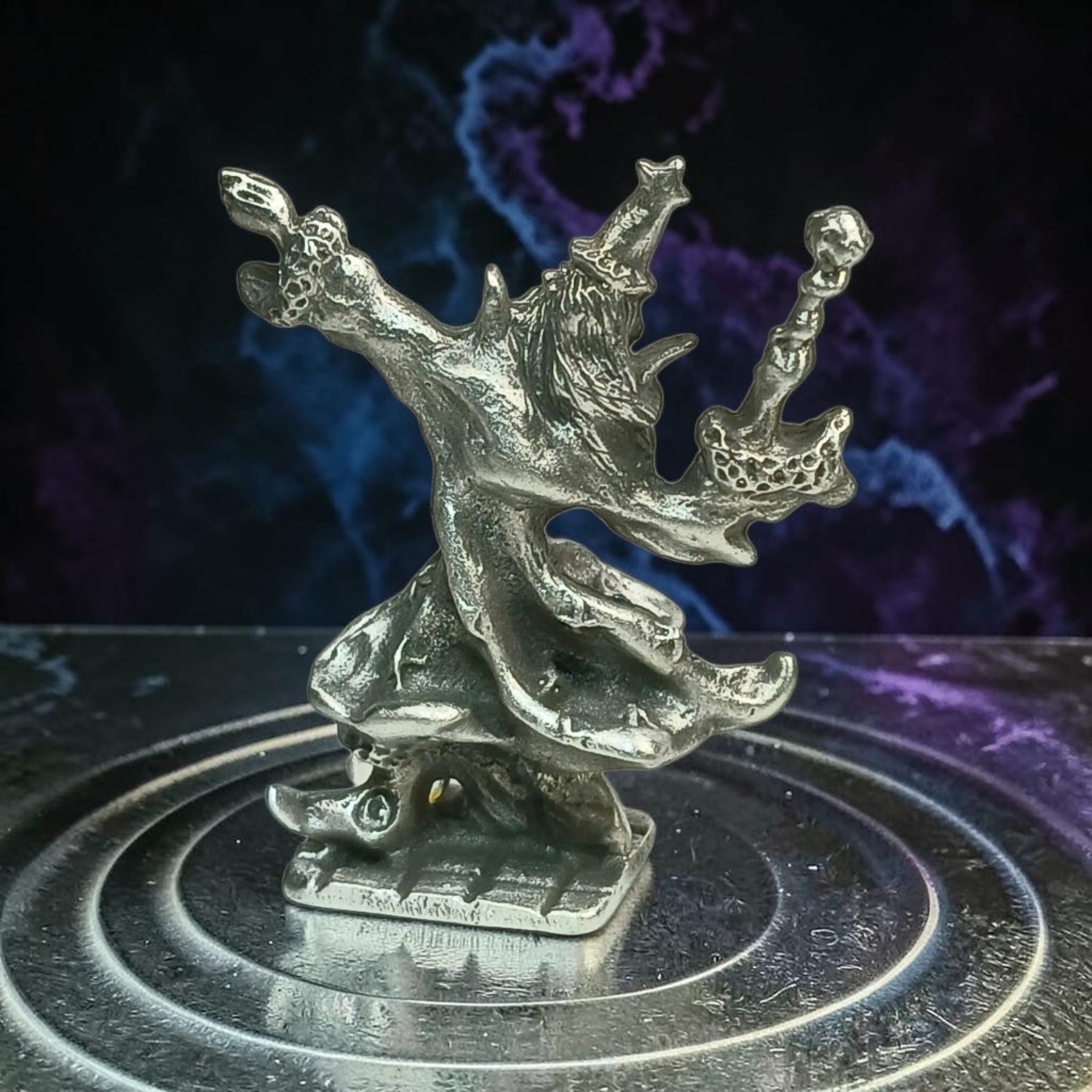 Another view of the pewter wizard with raised arms and sweeping robes, on a circular stand against a blue and purple background.